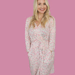 Woman wearing the Blooms & Bows Women’s Dream Robe with floral design, smiling against a pink background.