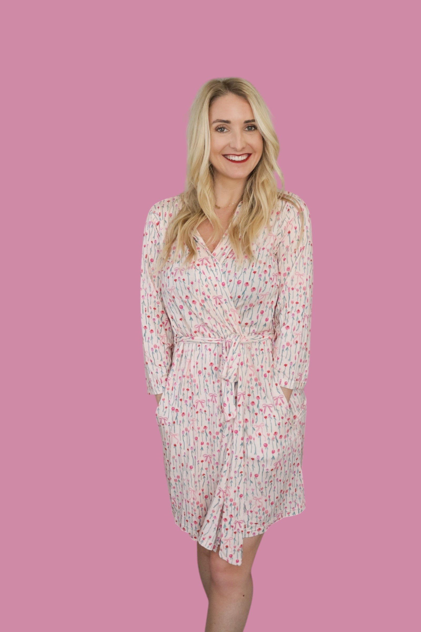 Woman wearing the Blooms & Bows Women’s Dream Robe with floral design, smiling against a pink background.
