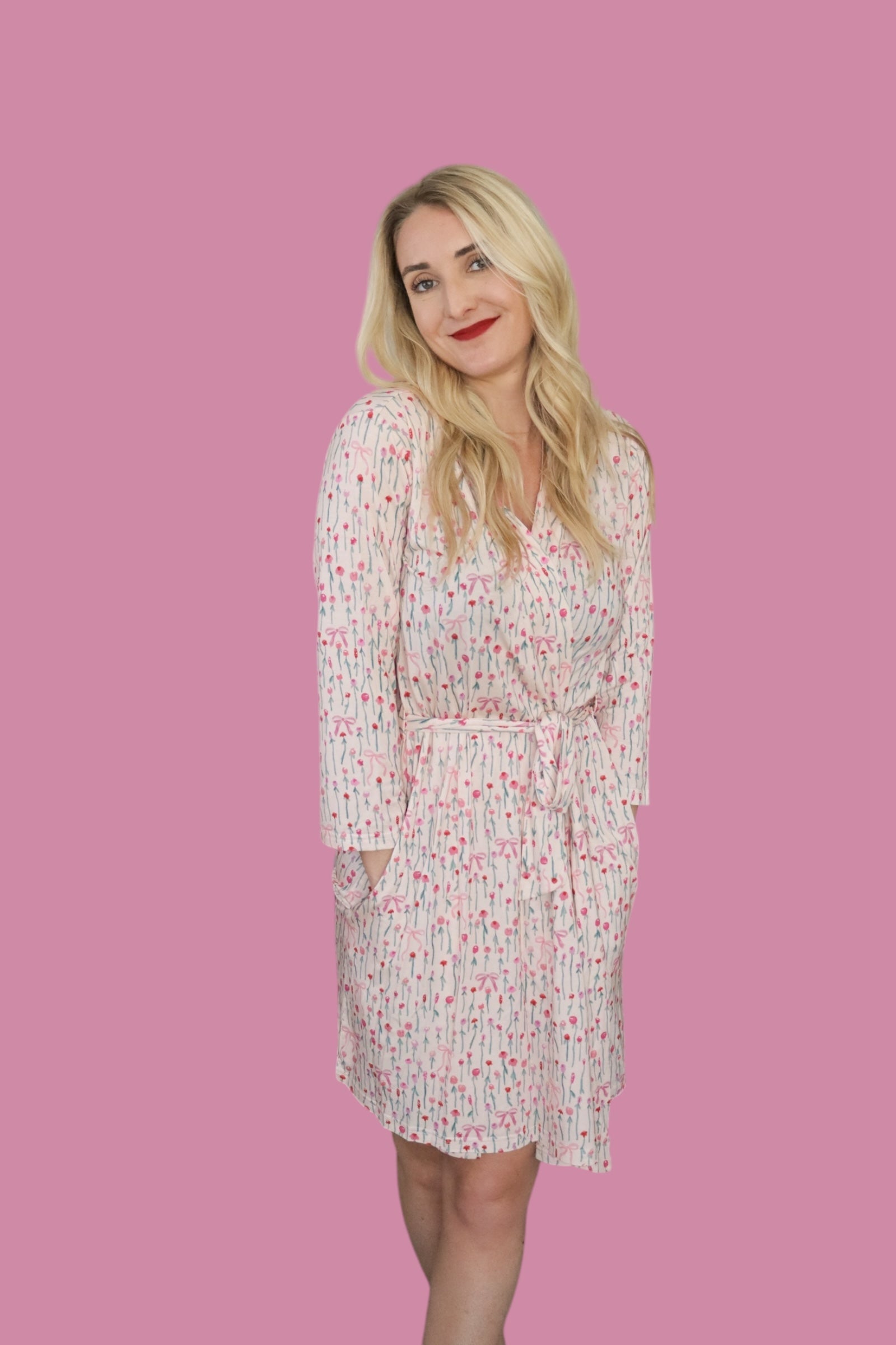 Woman wearing the Blooms & Bows Women's Dream Robe, featuring floral patterns and a tie waist, against a pink background.