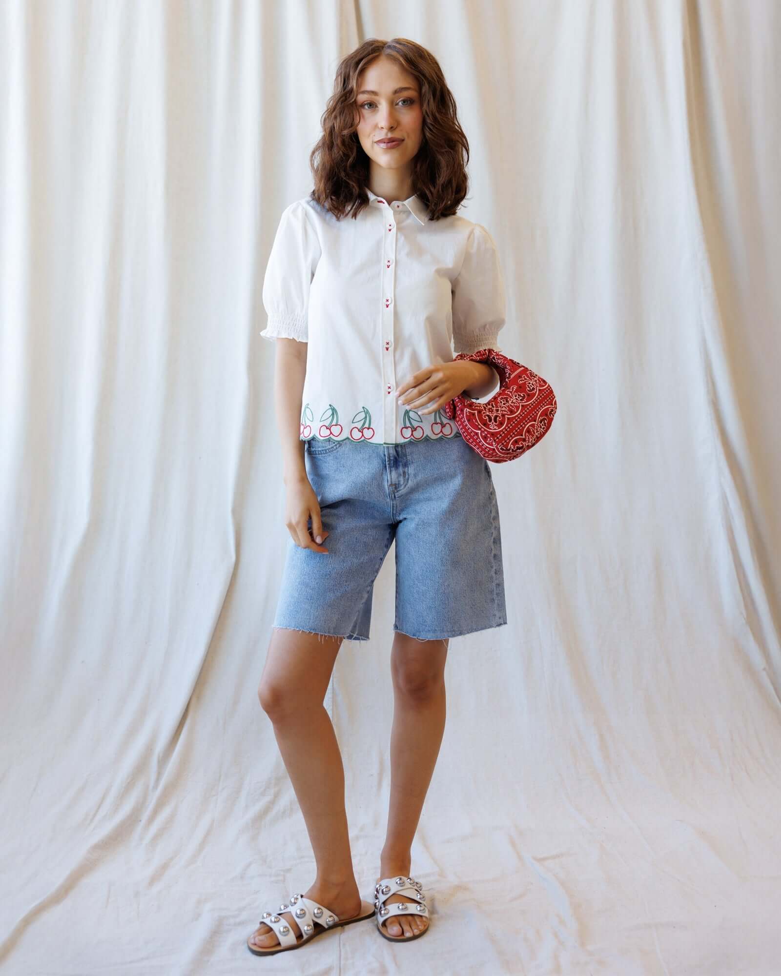 Model wearing Cherry Cute Button Down with puff sleeves, showcasing cherry embroidery and a stylish red bag.