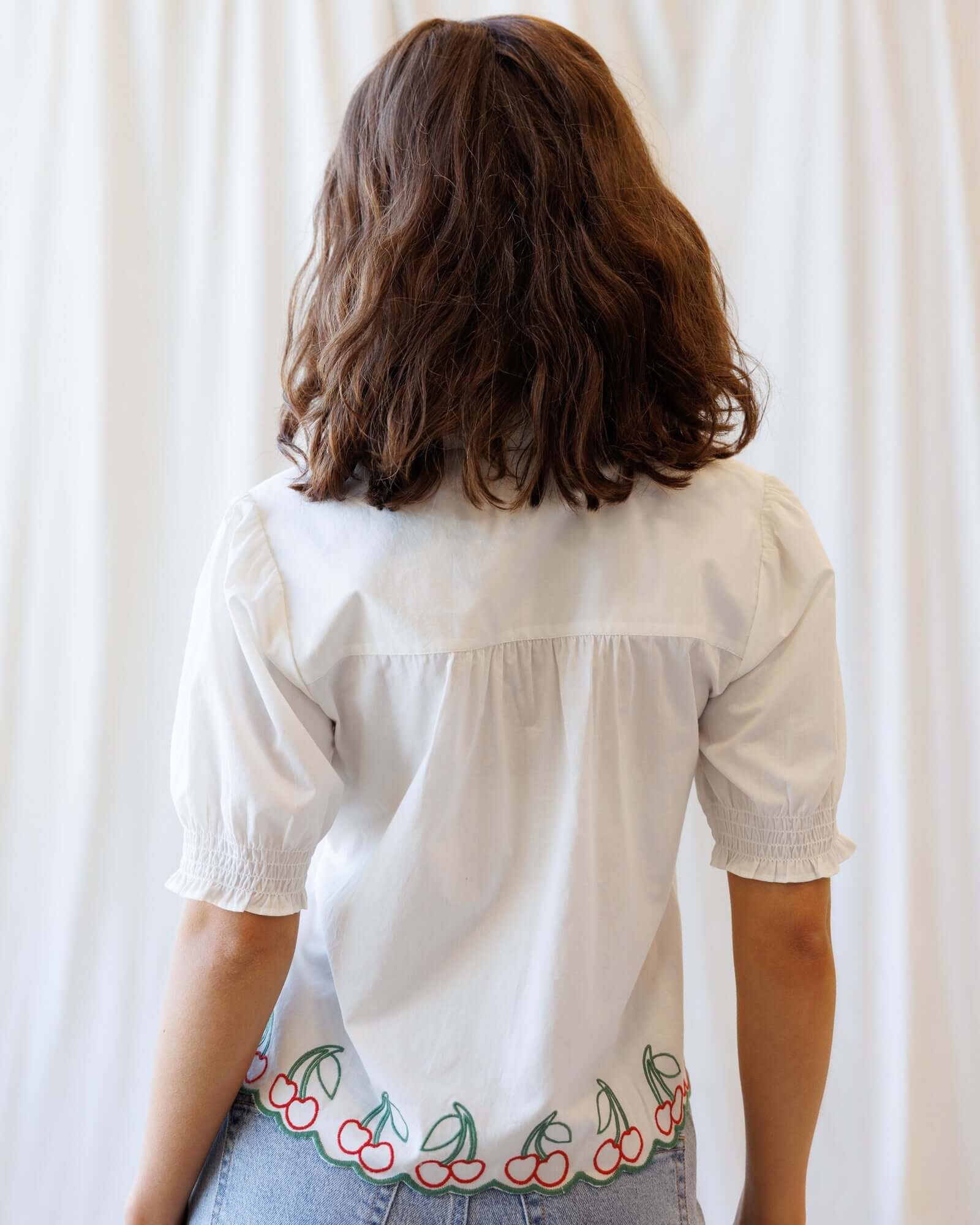 Back view of a woman wearing the Cherry Cute Button Down with cherry embroidered scallop hem.