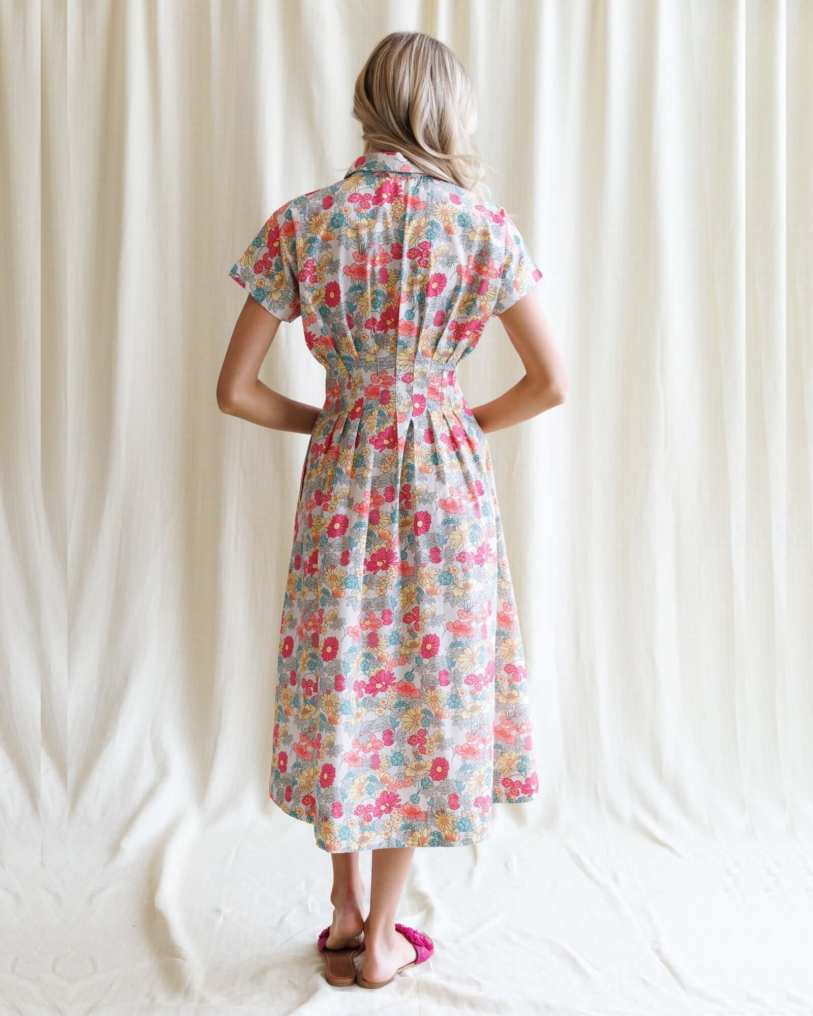 Back view of a woman in a floral Pleated Shirtdress, featuring a collared neckline and stylish waist pleats.