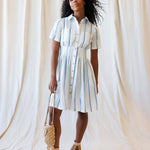 Model wearing a Seaside Stripe Dress with collared neckline, button-down front, and relaxed pleated skirt.