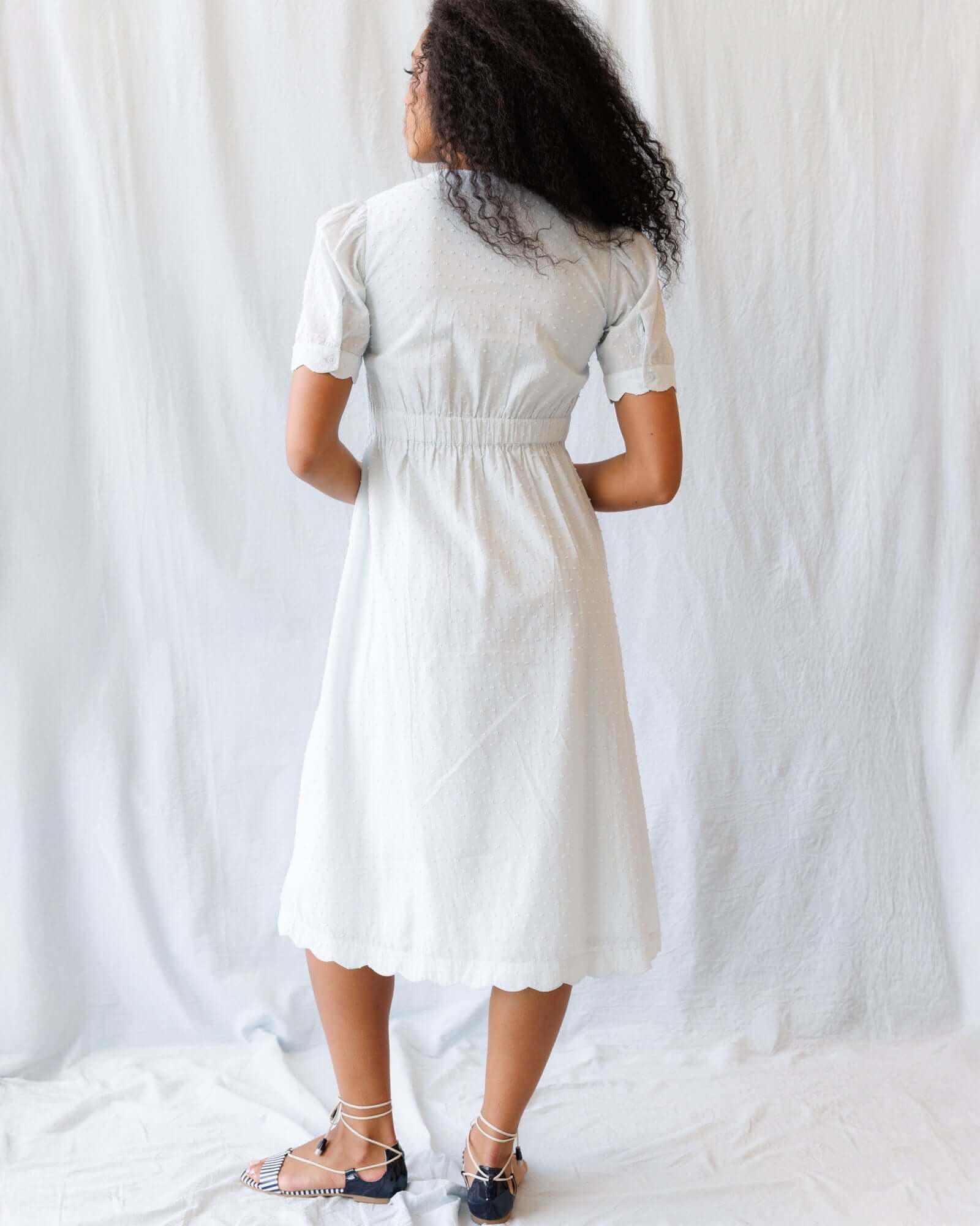 Back view of a woman wearing a Swiss Dot Scallop Dress with puff sleeves and a midi length skirt, perfect for nursing.