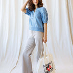 Model wearing Portside Chambray Popover with short puff sleeves, styled with casual pants and a tote bag.
