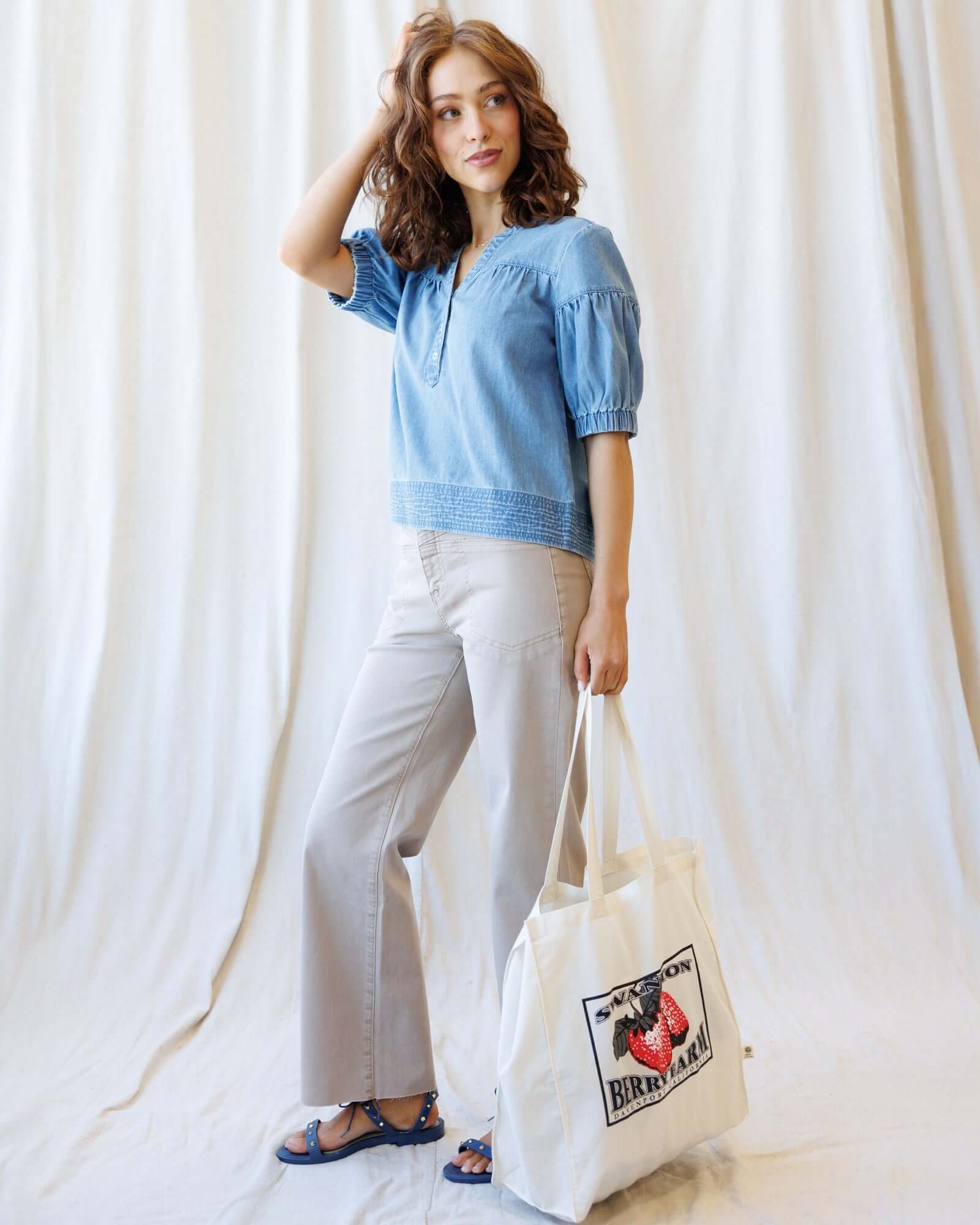Model wearing Portside Chambray Popover with short puff sleeves, styled with casual pants and a tote bag.
