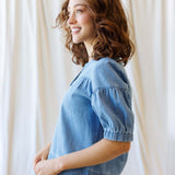 Side view of a woman wearing the Portside Chambray Popover with short puff sleeves, showcasing its relaxed fit.
