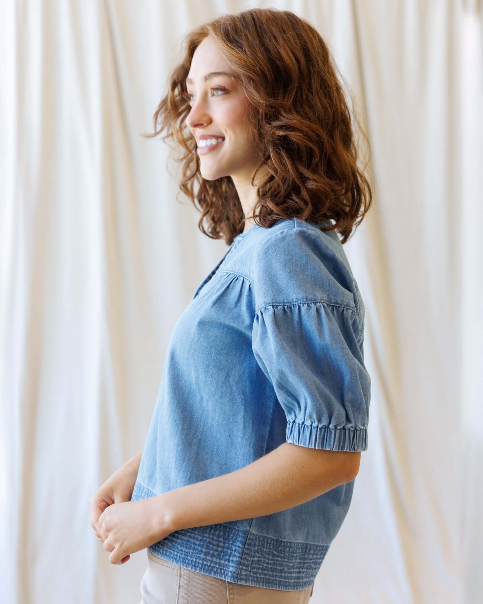 Side view of a woman wearing the Portside Chambray Popover with short puff sleeves, showcasing its relaxed fit.