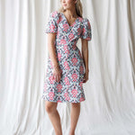 Woman wearing a floral dress standing against a white curtain