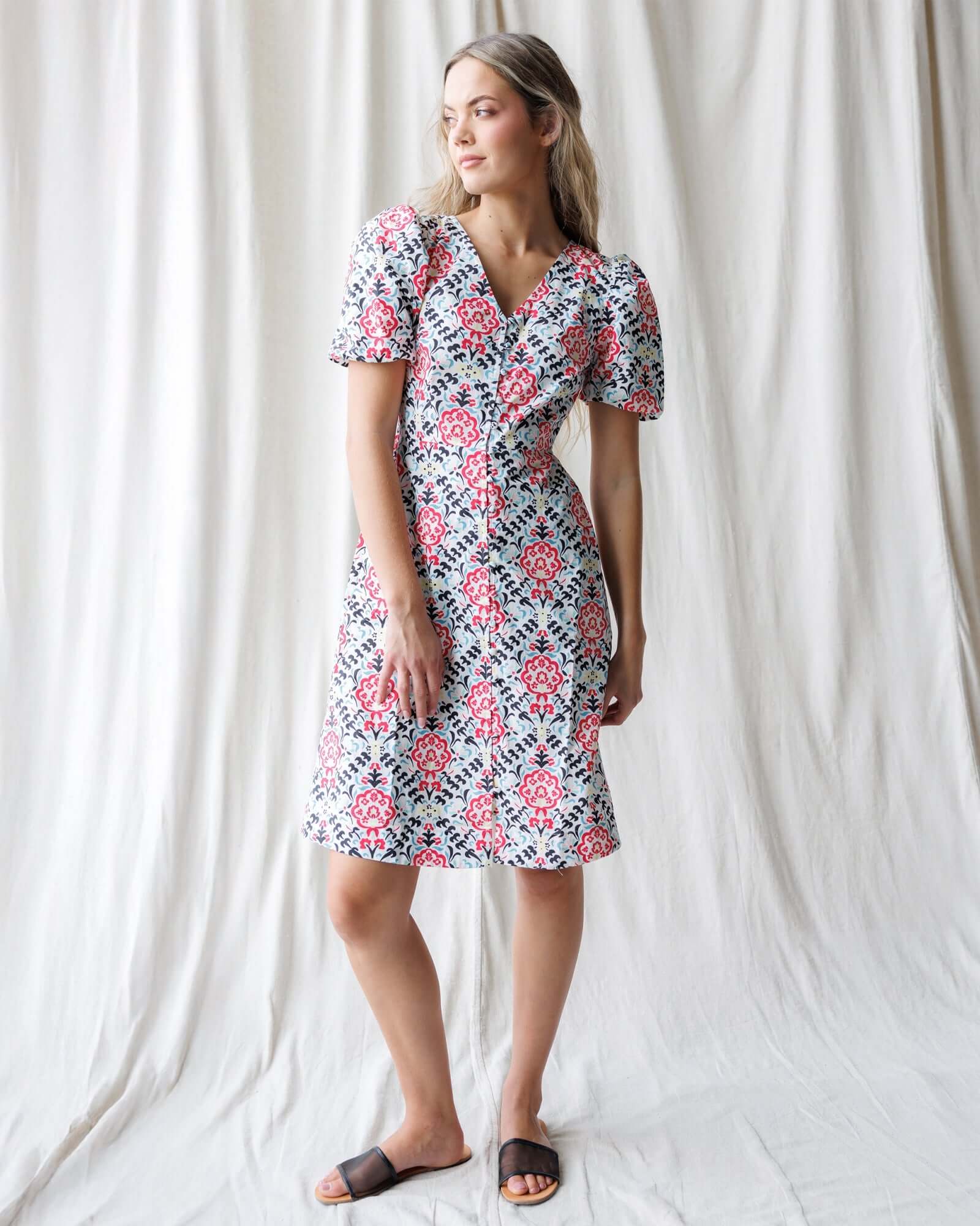 Woman wearing a floral dress standing against a white curtain