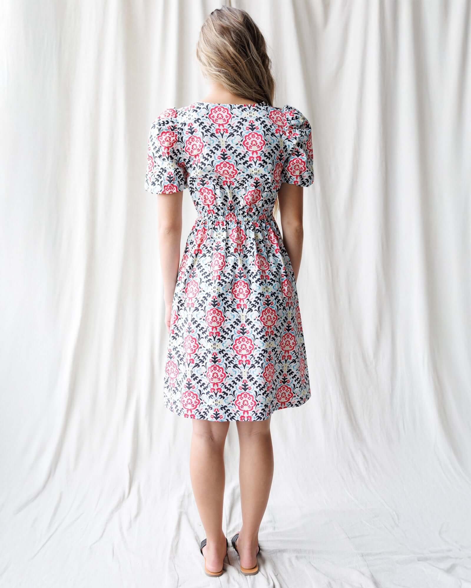 Back view of a model wearing a floral Capri Dress with puff sleeves, perfect for nursing friendly style with Milk & Baby.