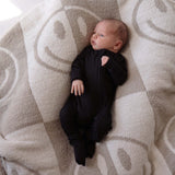 Baby in a black onesie lying on a textured beige blanket