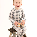 Happy child wearing Slate Gingham | Zip Romper, sitting on a stool holding toy trucks, showcasing adorable design.