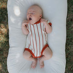A baby yawning in a Picnic Pinstripe | Knit Romper, featuring soft knit fabric and warm checkerboard stripes.