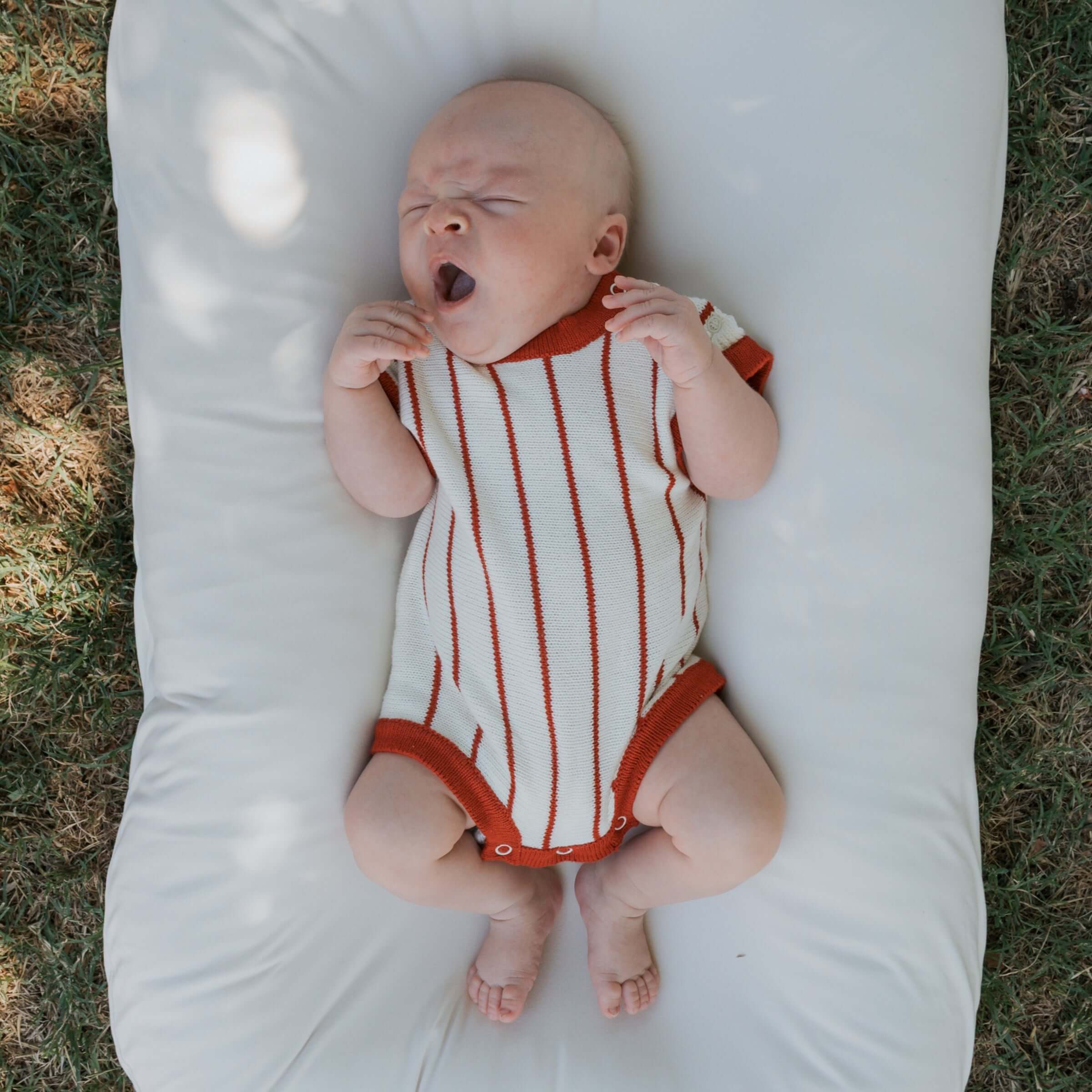 A baby yawning in a Picnic Pinstripe | Knit Romper, featuring soft knit fabric and warm checkerboard stripes.