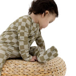 Toddler wearing Sage Check | Zip Romper sitting on a woven pouf, showcasing soft bamboo blend fabric.