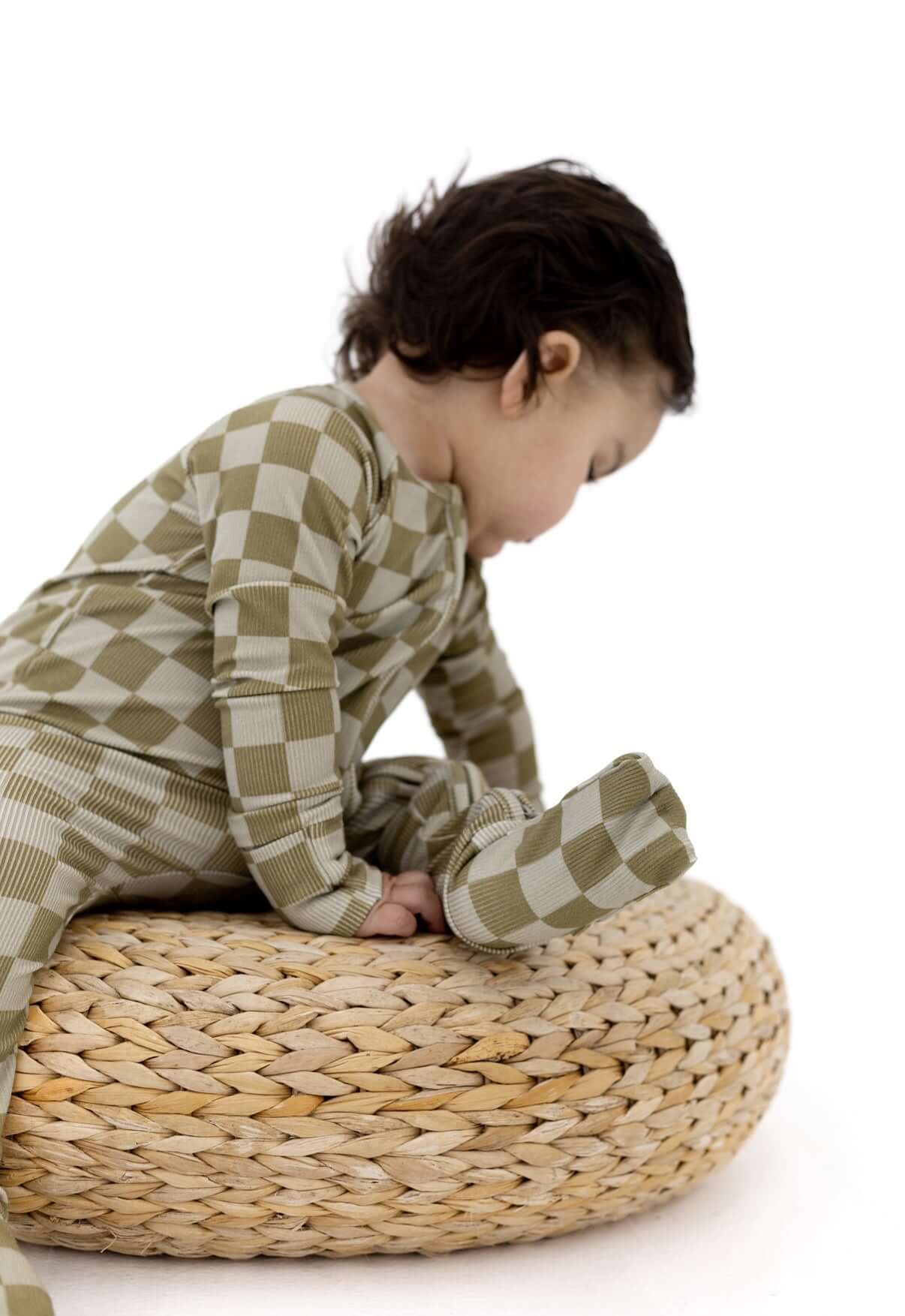 Toddler wearing Sage Check | Zip Romper sitting on a woven pouf, showcasing soft bamboo blend fabric.