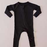 Black baby onesie with a zipper on a light beige background