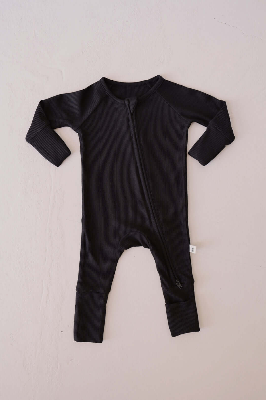 Black baby onesie with a zipper on a light beige background