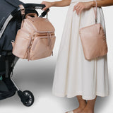 Caraa Baby Bag in blush nylon hanging from stroller, held by a woman in a white skirt, showcasing its design and functionality.