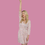 Model wearing Blooms & Bows Women’s Dream Robe with floral design, raising one arm in a playful pose against a pink background.