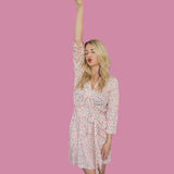 Model wearing Blooms & Bows Women’s Dream Robe with floral design, raising one arm in a playful pose against a pink background.