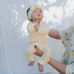 Baby wearing Veda Bamboo Zip Pajamas in yellow with polka dots, held by an adult in a lemon print top.