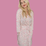 Woman wearing the Blooms & Bows Women's Dream Robe, featuring floral patterns and a tie waist, against a pink background.