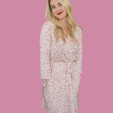 Woman wearing the Blooms & Bows Women's Dream Robe, featuring floral patterns and a tie waist, against a pink background.