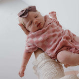 Baby in pink checkered outfit with bow headband on a white background