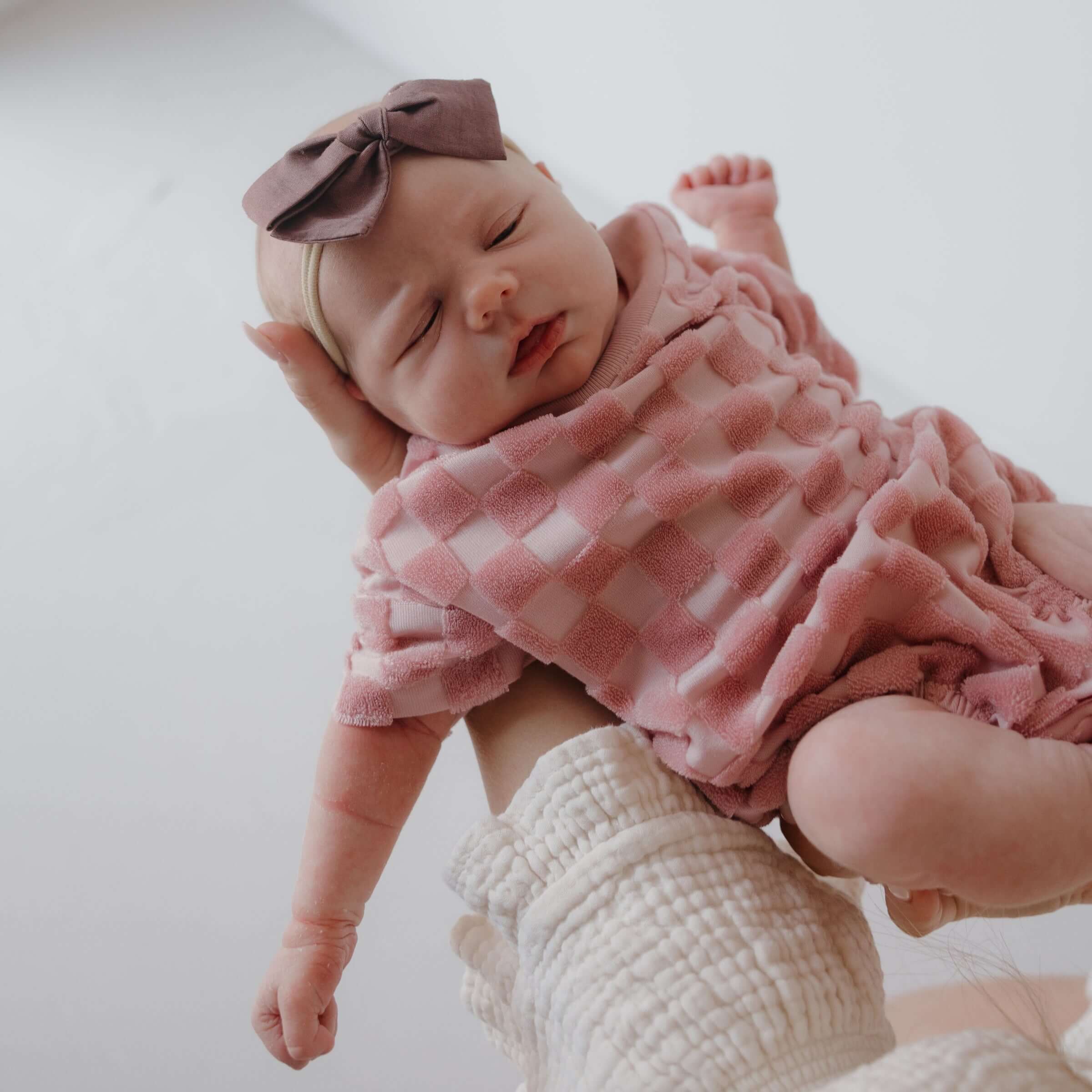 Baby in pink checkered outfit with bow headband on a white background