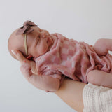 Newborn baby in pink checkered outfit with headband on a light background
