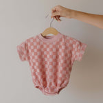 Pink checkered baby romper on a hanger against a plain background