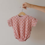 Pink checkered baby romper on a hanger against a plain background