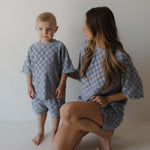 Woman and child wearing matching gray blue checkered outfits against a plain background
