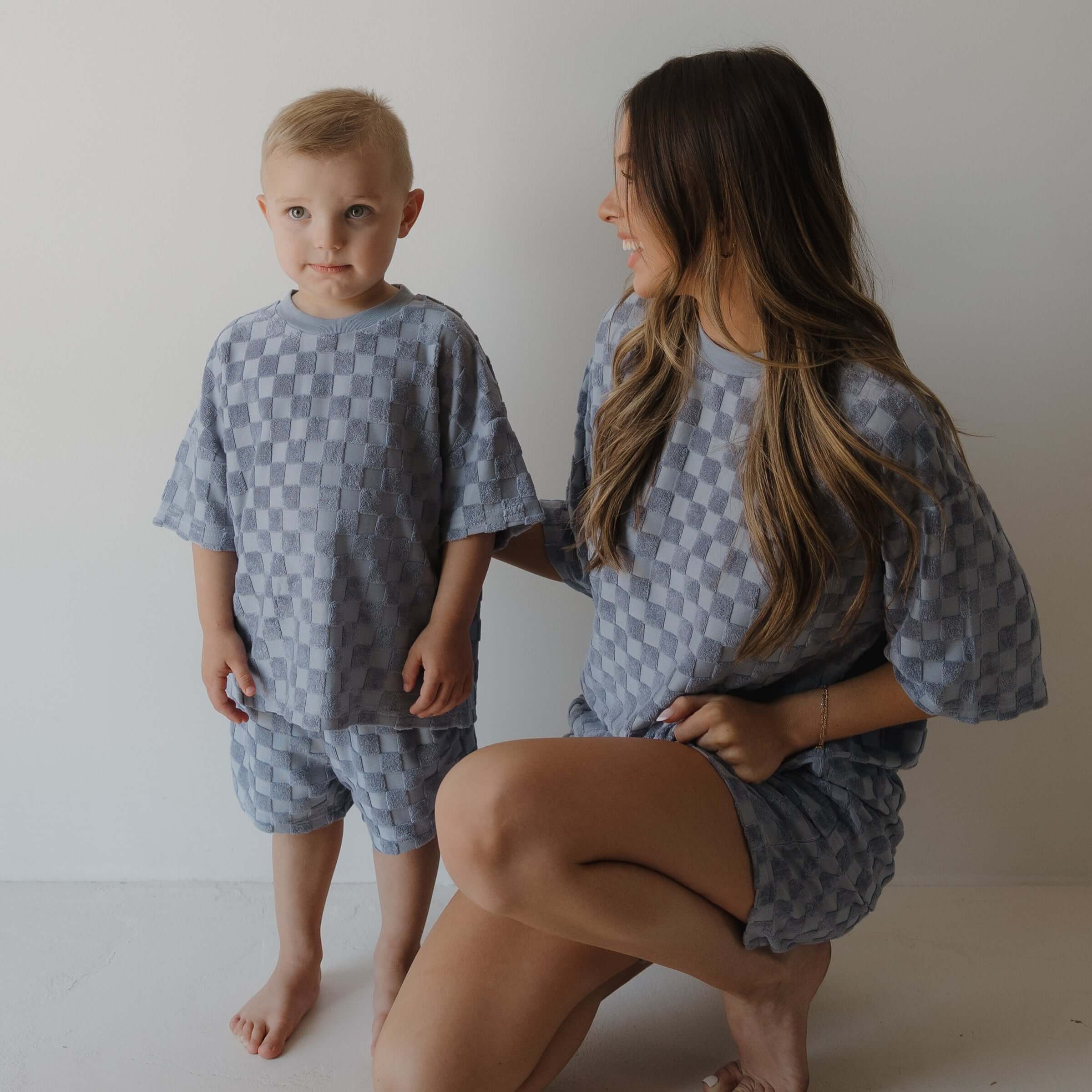 Woman and child wearing matching gray blue checkered outfits against a plain background