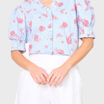 Woman wearing a blue floral blouse with white shorts on a plain background