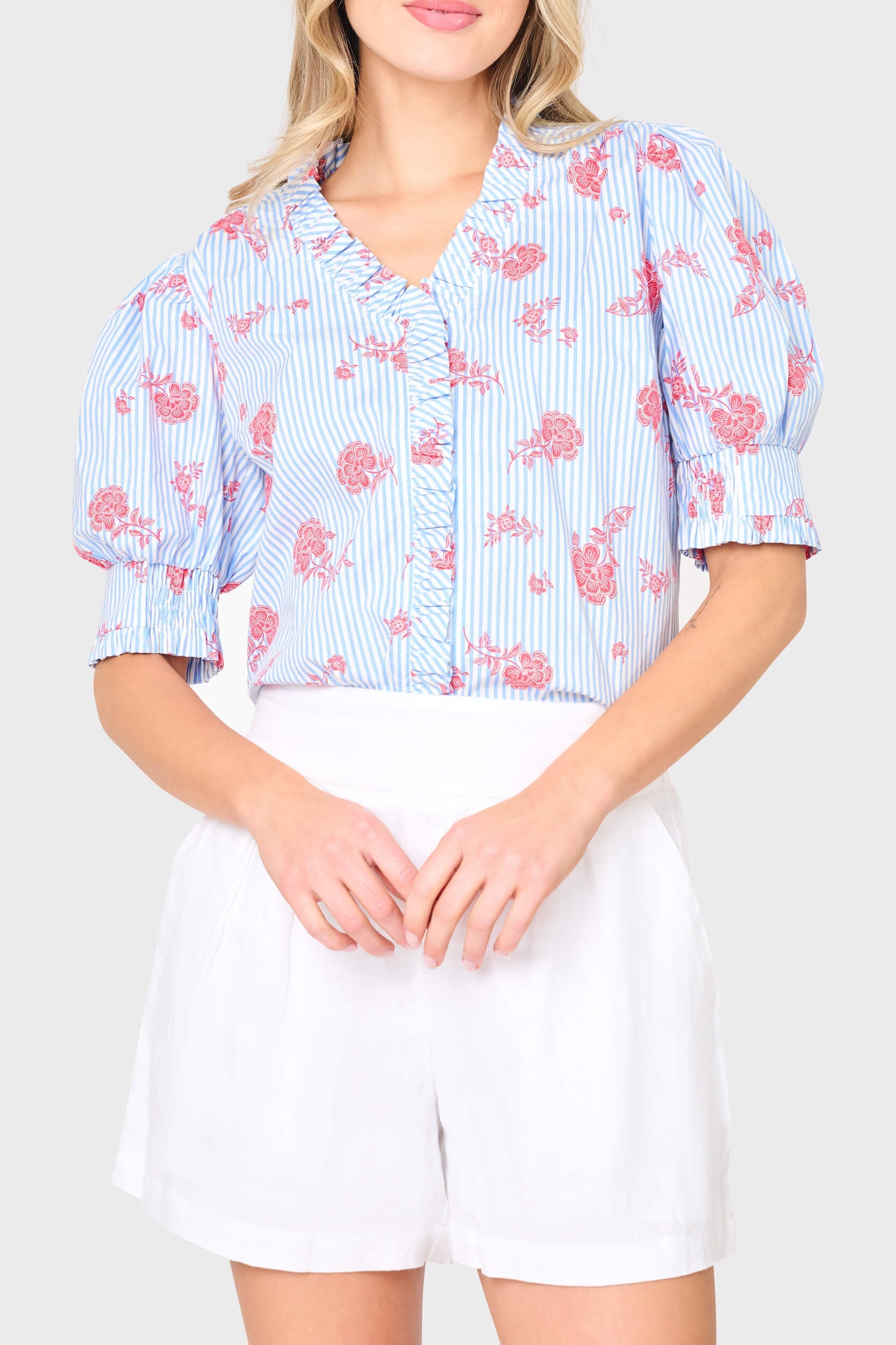 Woman wearing a blue floral blouse with white shorts on a plain background