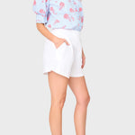 Woman wearing a light blue floral blouse and white shorts on a plain background