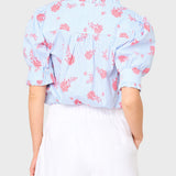 Woman wearing a light blue floral blouse with pink flowers on a white background
