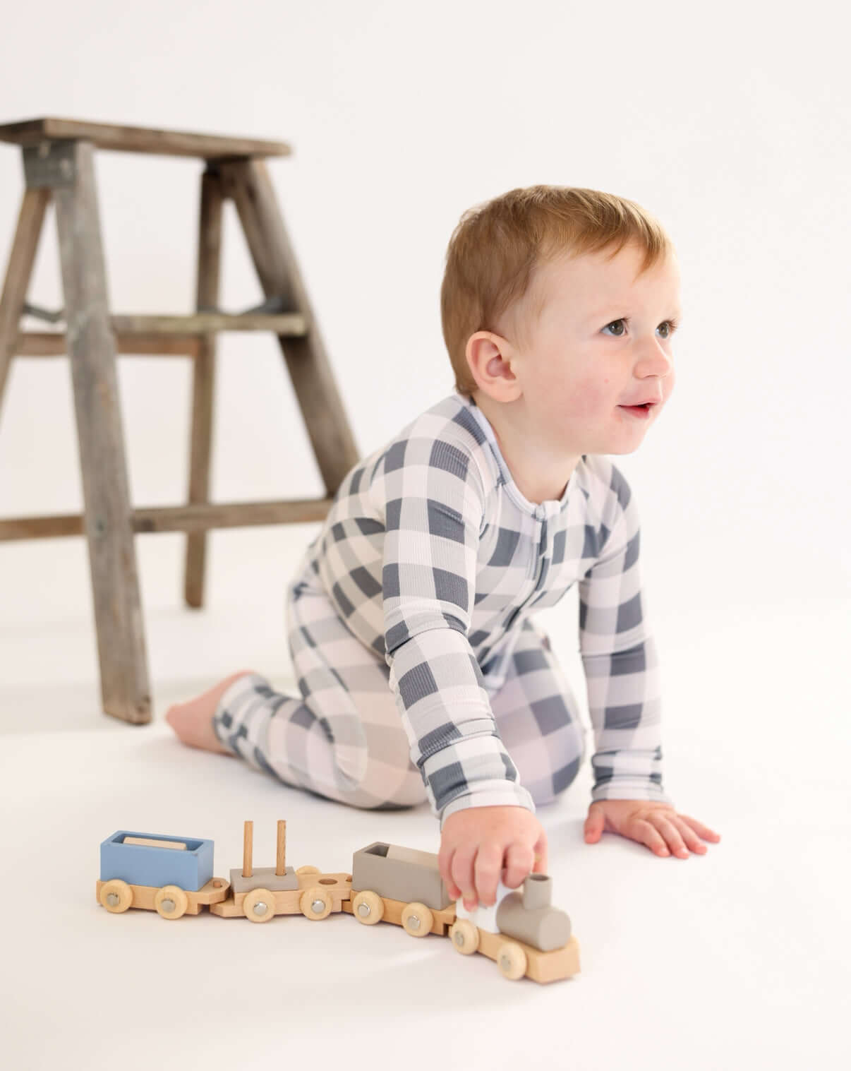 Toddler playing with wooden train while wearing Slate Gingham | Zip Romper, showcasing comfort and style.