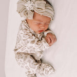 Newborn baby wearing a patterned outfit and headband with flowers on a white background