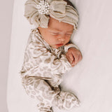 Newborn baby wearing a patterned outfit and headband with flowers on a white background