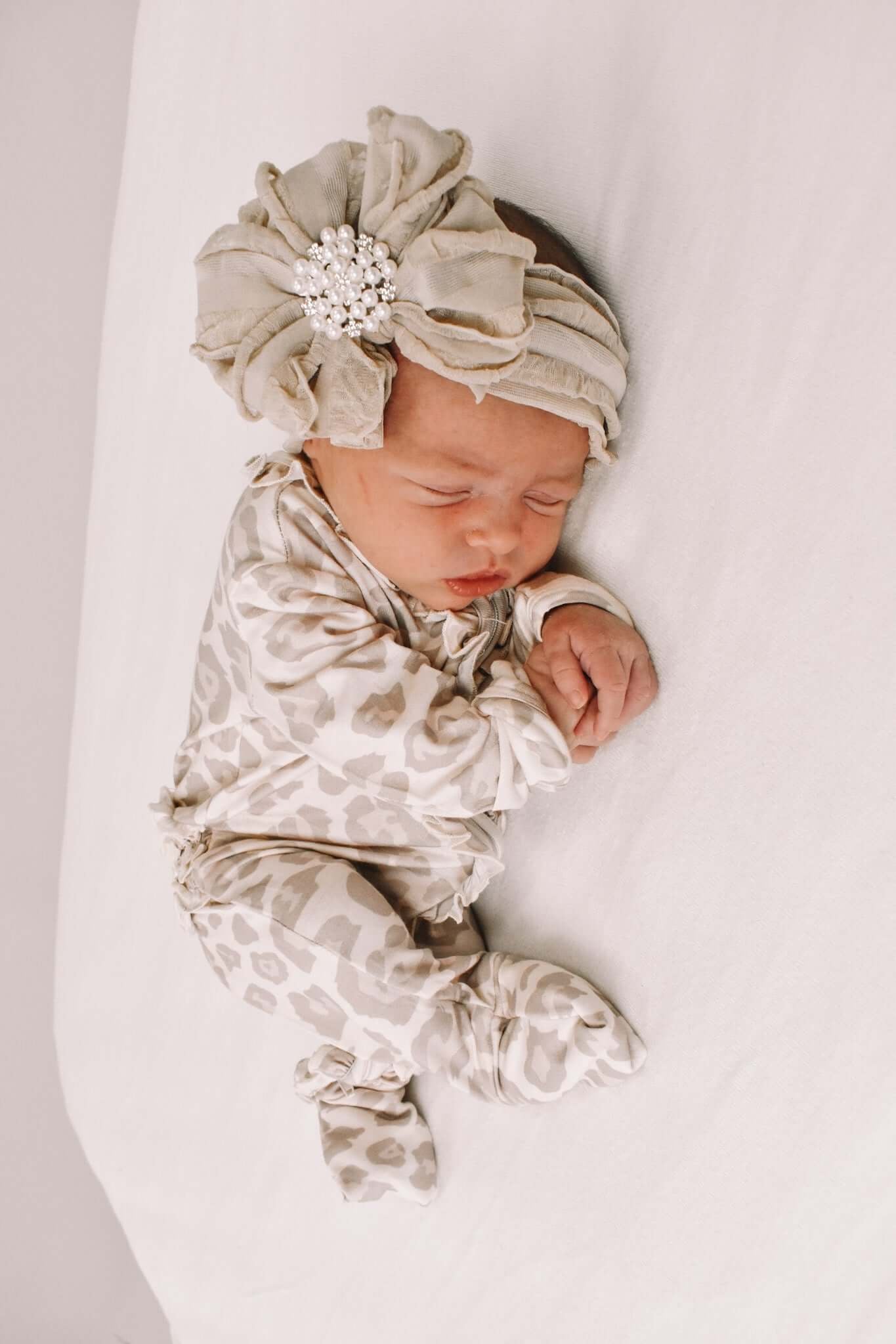 Newborn baby wearing a patterned outfit and headband with flowers on a white background