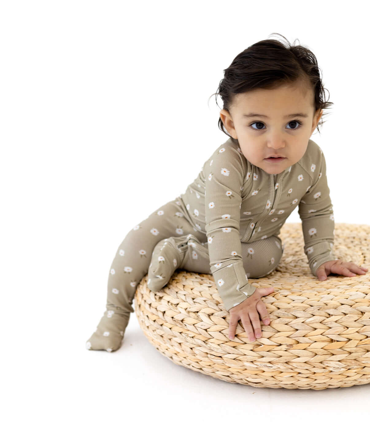 Cute baby in a Sage Floral | Zip Romper sitting on a comfy round basket.