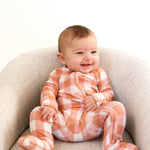 Happy baby wearing a Coral Gingham Zip Romper, featuring soft fabric and convenient double zipper for diaper changes.