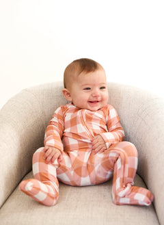 Happy baby wearing a Coral Gingham Zip Romper, featuring soft fabric and convenient double zipper for diaper changes.