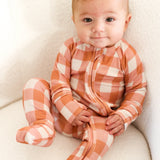 Baby wearing Coral Gingham Zip Romper with fold over cuffs, sitting comfortably on a soft surface.