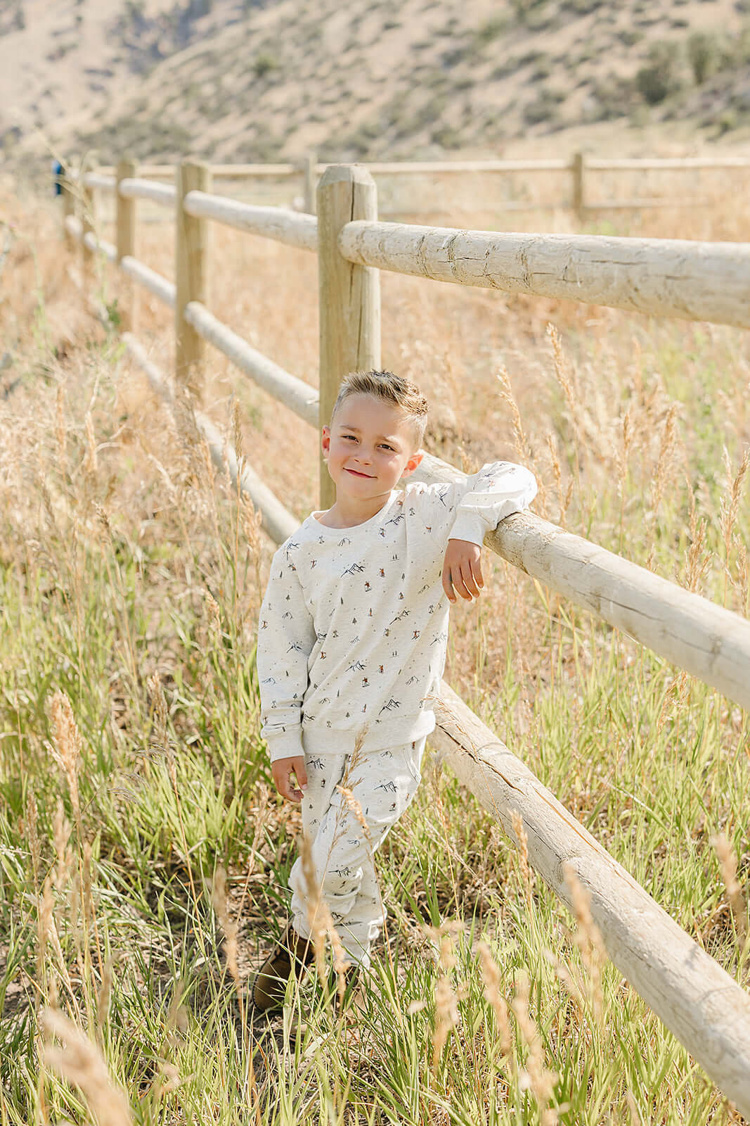 Young boy in Mebie Baby Skier French Terry Set enjoying the outdoors next to a wooden fence.