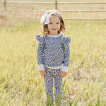 Little girl in a Blue Meadow Ruffle French Terry Set standing in a grassy field, showing off the charming floral design.